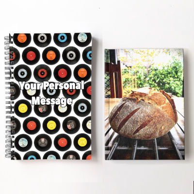 two notebooks side by side, one featuring some vinyl records in a mosaic pattern and the other notebook showing a large loaf of bread on a kitchen table