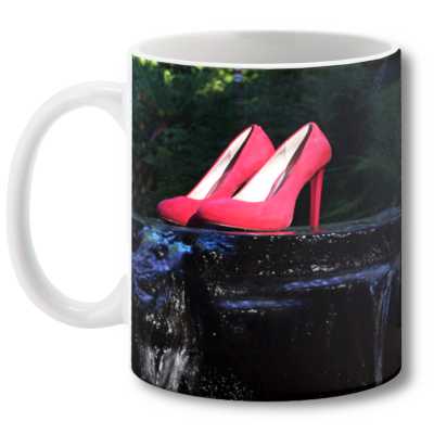 A coffee mug showing an image on it, the image having a pair of pink high heel shoes sat upon some flowing water