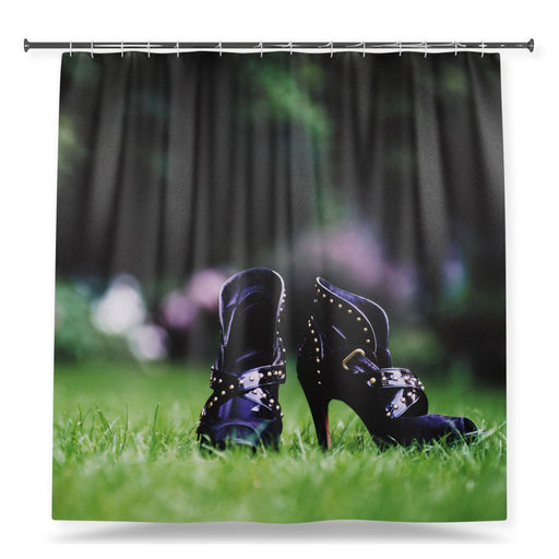 A shower curtain showing an image of a pair of purple high heel ankle boots sat on a green grassy lawn, with a white background
