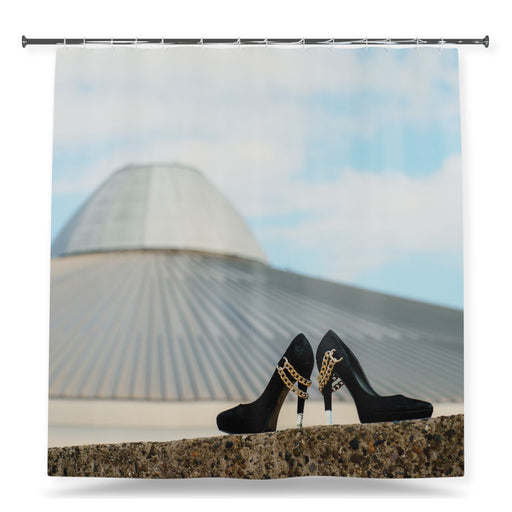 A shower curtain showing an image of a pair of high heel shoes sat on a wall in front of a city skyline, with a white background
