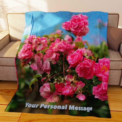 A fleece blanked draped over a couch, the blanket having an image of pink roses on it along with a personalised text message