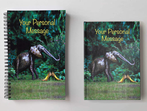 Two notebooks, side by side, both having covers with an image of a pair of yellow high heel shoes adjacent to a small metal elephant, set within a garden, with a personal message on the cover