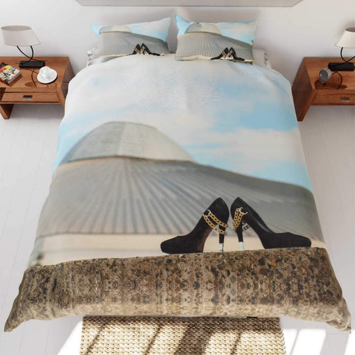 A duvet cover on a bed, the duvet cover having an image of a building skyline with a pair of shoes in the foreground, the building has the shape of a UFO