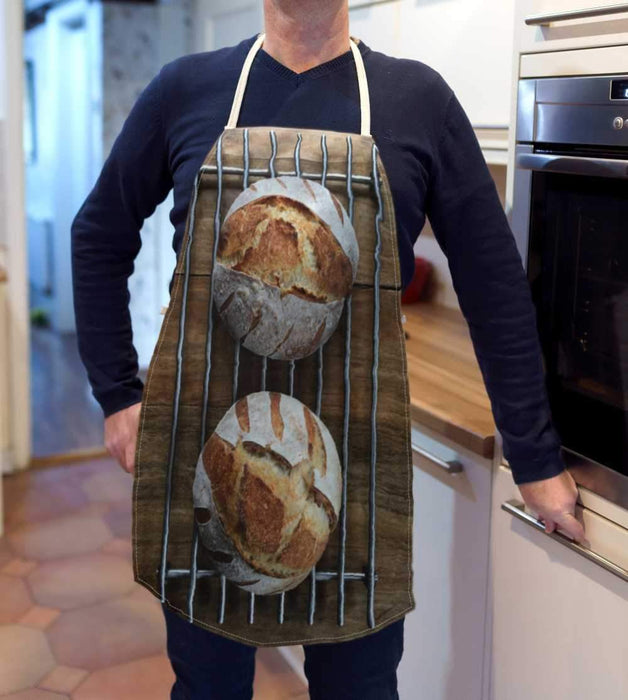A kitchen apron being worn by a man in a kitchen, the apron having an image of a large sourdough loaf two sourdough loaves seen from above