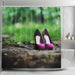 image of a shower curtain adjacent to a bath, the curtain having an image of a pair of purple high heel shoes on a path in the woods