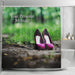 image of a shower curtain adjacent to a bath, the curtain having an image of a pair of purple high heel shoes on a path in the woods, along with a printed personal message