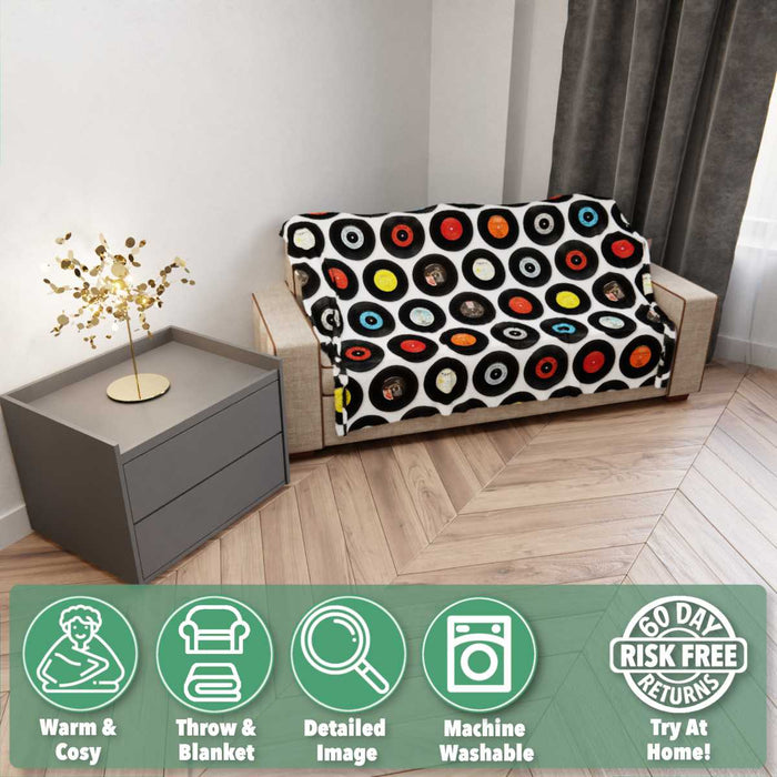 A blanket draped over a couch, the blanket haviing images of vinyl records on it, the couch is in a room with a wooden floor and there is overlay text on the image describing the details of the blanket