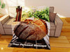 a fleece blanket flat on the couch, the blanket having an image of a sourdough loaf of bread sat upon a table in a kitchen, along with a printed personal message