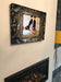 A  canvas print hung above a fire, the print of a mirror showing a pair of orange high heel stiletto shoes in the reflection, the mirror has a dark brass etched surround on it