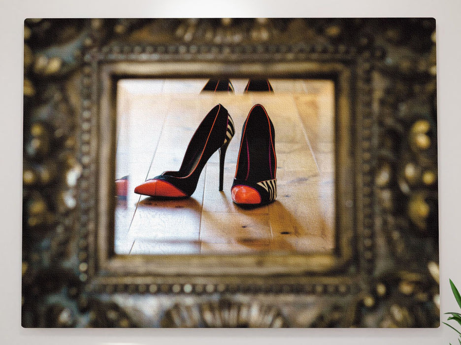 A mirror showing a pair of orange high heel stiletto shoes in the reflection, the mirror has a dark brass etched surround on it
