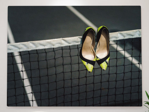 A pair of yellow high heel stiletto shoes hung on a tennis net