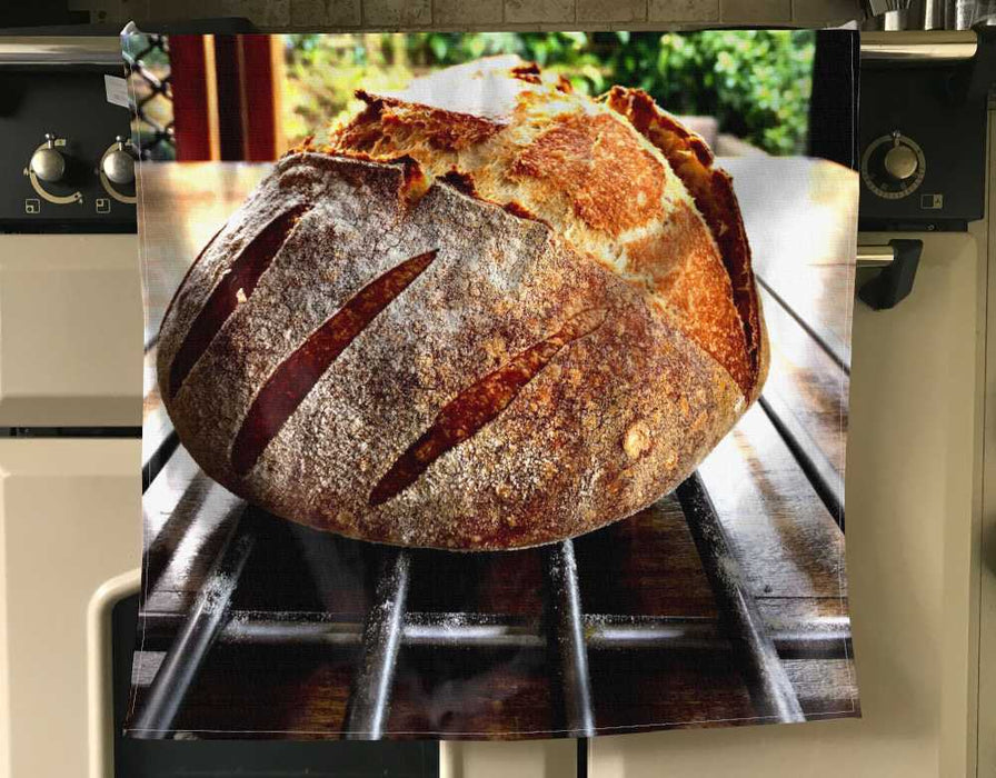 An apron draped over a kitchen cooker, the apron having an image of a large sourdough loaf on it
