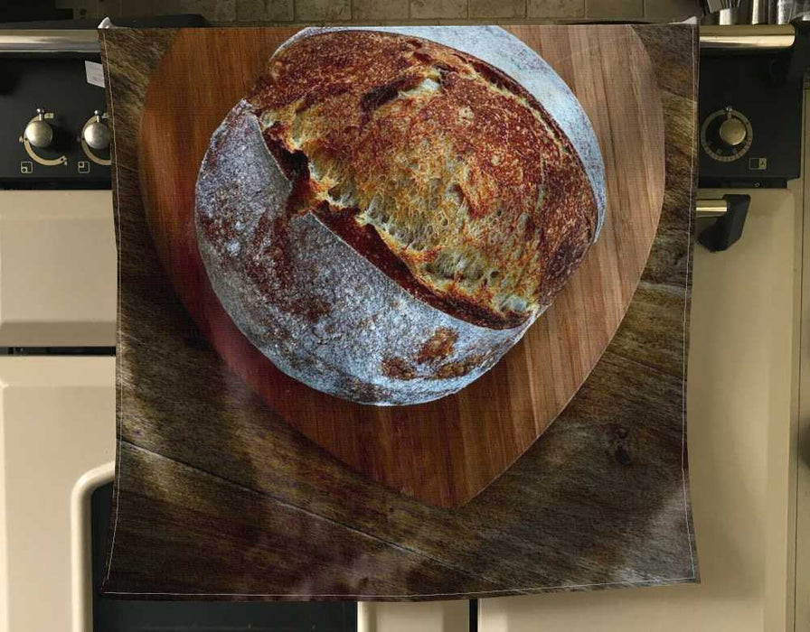 image of an apron hung next to a kitchen cooker, the apron has an image of a sourdough loaf of bread on it
