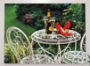 A canvas print hung above a couch with the print showing a pair of shoes on a garden table adjacent to an opened bottle of champagne or prosecco