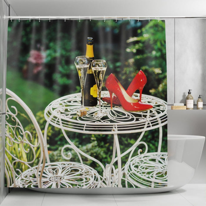 A shower curtain in a bathroom, the curtain having an image of a pair of red high heel shoes sat on a garden table next to a bottle of sparkling wine and two full glasses