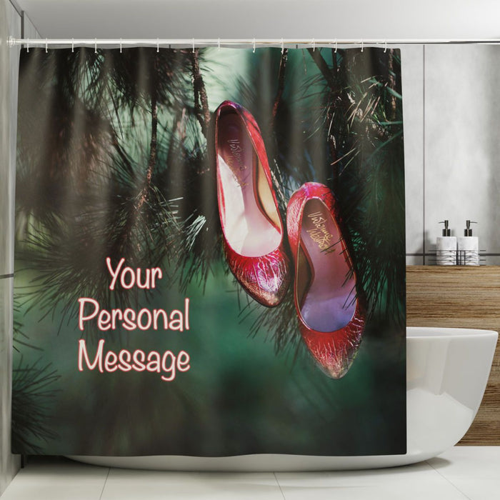 A shower curtain in a bathroom, the curtain having an image of a pair of red high heel shoes hanging of the branch of a tree, along with a personal message printed on the curtain