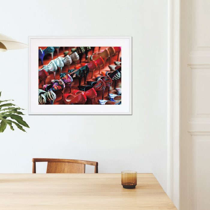 A framed print with a white frame hung on the walls of a kitchen, the print showing a multiple rows of high heel shoes all of different colours