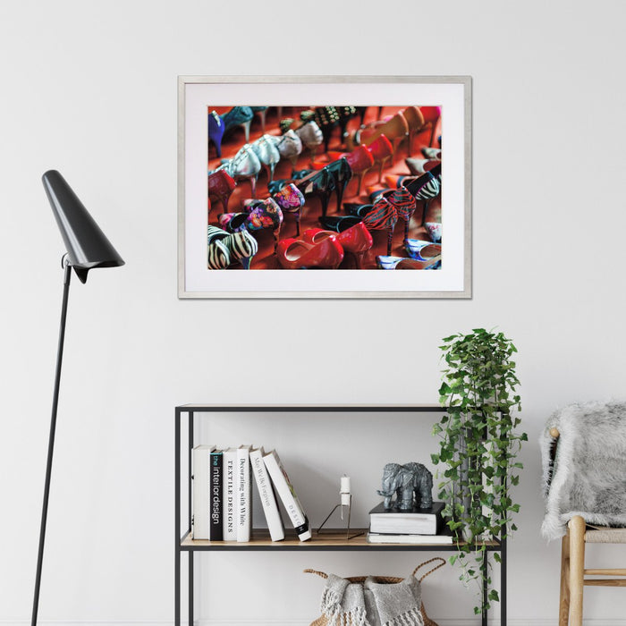 A framed print with a silver frame hung o the walls of a living room, the print showing a multiple rows of high heel shoes all of different colours