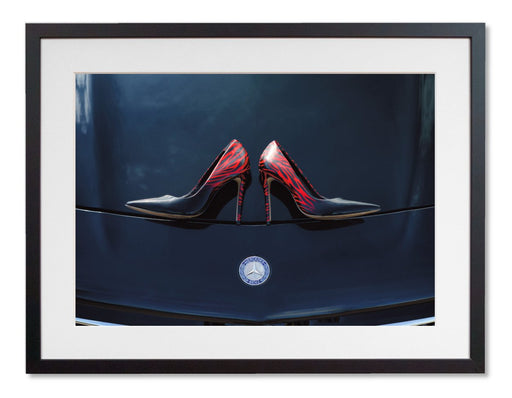 A framed print with a black frame, the print showing a pair of purple high heel shoes on the bonet of a high performance car