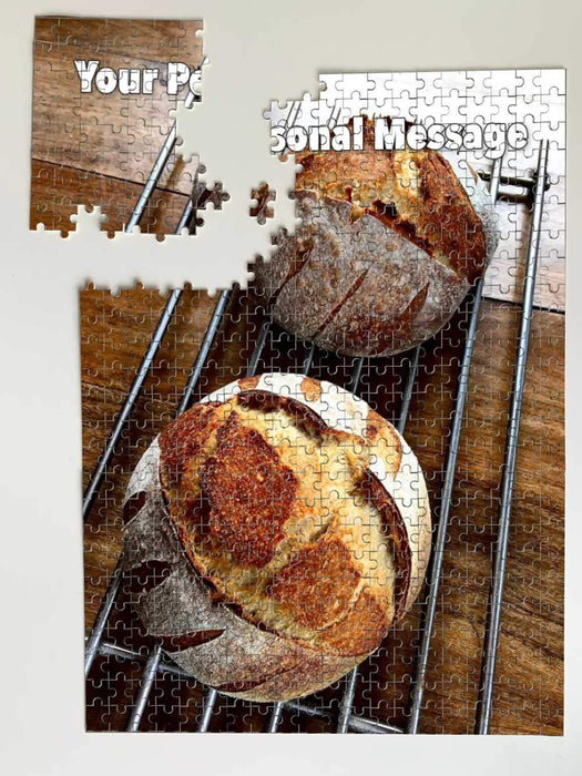 A partially broken jigsaw showing an image of two sourdoughs loaves siting on a wire tray along with a personalised message on the jigsaw