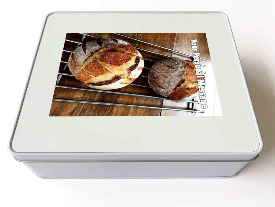 A white tin, upon which is an image of two sourdoughs loaves siting on a wire tray along with a personalised message on the jigsaw
