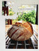 A partially broken jigsaw showing an image of a large sourdough loaf on  a table with a garden visible behind through the window