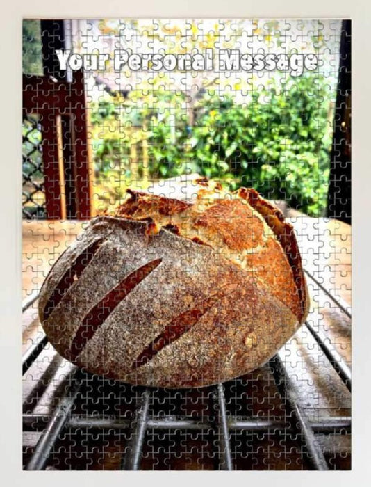 A jigsaw showing an image of a large sourdough loaf on  a table with a garden visible behind through the window