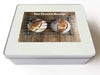 A white tin box, upon the lid is an image of two sourdough loaves seen from directly overhead, the loaves sitting on a metal tray along with a printed personal message