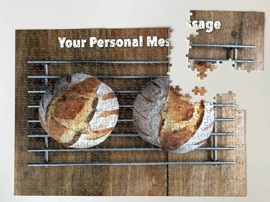 A partially broken jigsaw with an image of two sourdough loaves seen from directly overhead, the loaves sitting on a metal tray along with a printed personal message