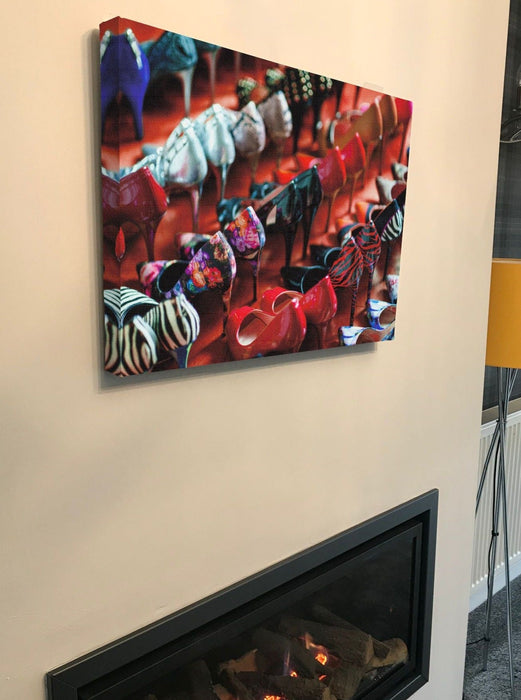 A canvas print hung on a wall above a fire, the print showing multiple rows of ladies high heel shoes