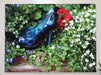 a pair of blue shoes sat in a flower bed, with green leaves and white flowers