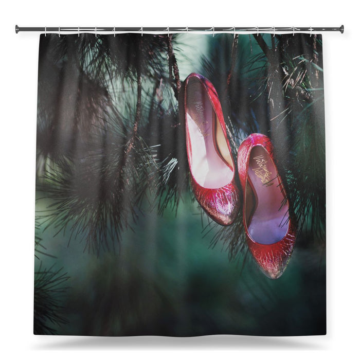 A shower curtain showing an image of a pair of red high heel shoes growing from the branch of a tree, with a white background