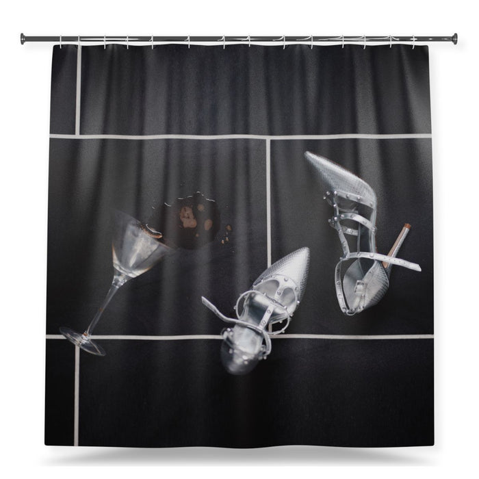 A shower curtain showing an image of a pair of silver high heel shoes lying on black tiled floor next to a spilt cocktail drink, with a white background