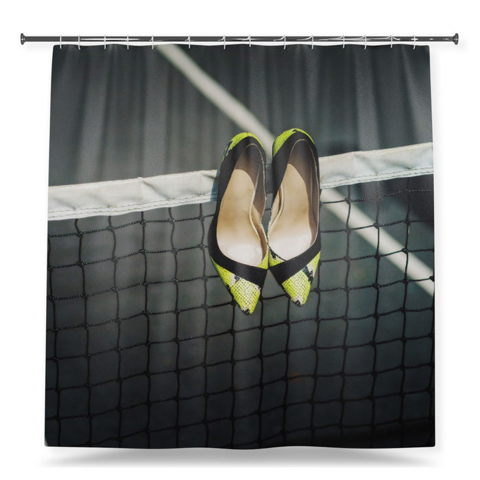 A shower curtain showing an image of a pair of black and yellow high heel shoes hung off a tennis net, with a white background