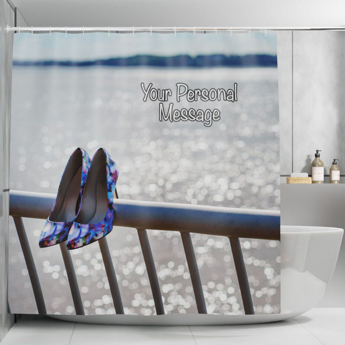 A shower curtain in a bathroom, the shower curtain having an image of a pair of purple high heel shoes hung on metail railings in front of the ocean, along with a printed personal message on the curtain