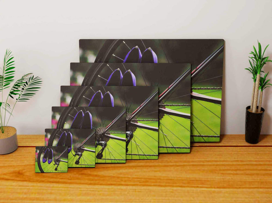 multiple canvas prints showing a bike with a pair of purple ladies heels hung off the rear wheel, each canvas being of a different size and they are laid against each other on  a wooden floor
