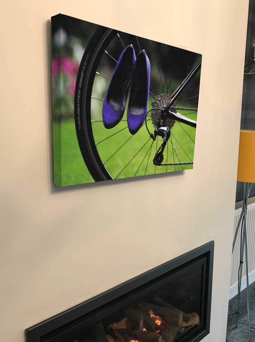 canvas print of the back of a bicycle with pair of purple shoes hung off the rear wheel, the canvas print hung on a chimney breast above a lit fire