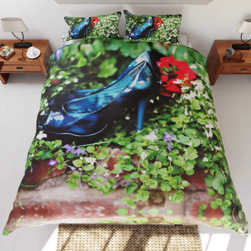 A bed with a duvet cover, the duvet having an image of a pair of blue high heel shoes surrounded by flowers