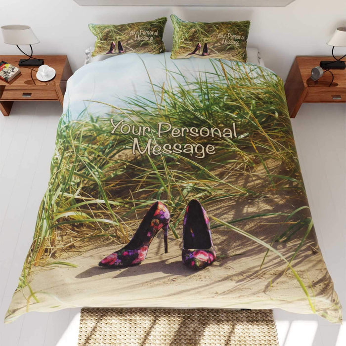 A duvet cover on a bed, the duvet cover having an image of a pair of high heel shoes on a beach near to some sandhills with grass and blue sky, the duvet is folded back to show a white underside
