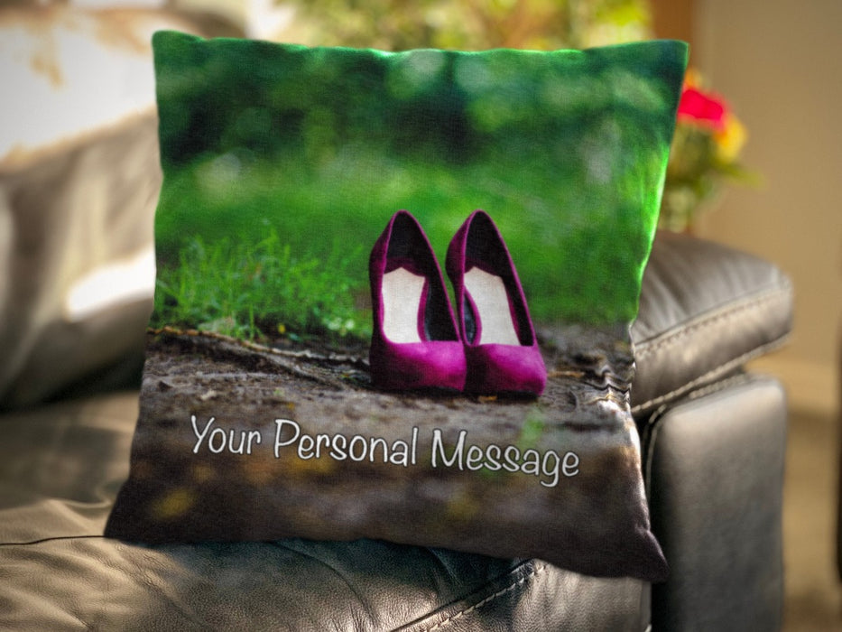 A cushion with an image of a pair of pruple high heels on a path through some woods, the cushion is resting on a couch, and there is a personal message printed on the cushion