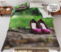 A duvet cover showing a pair of purple high heel shoes on a muddy path in a forest, the duvet is on a bed an seen from top and has a folded corner showing white underneath