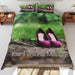 A duvet cover showing a pair of purple high heel shoes on a muddy path in a forest, the duvet is on a bed an seen from top along with a personal message printed