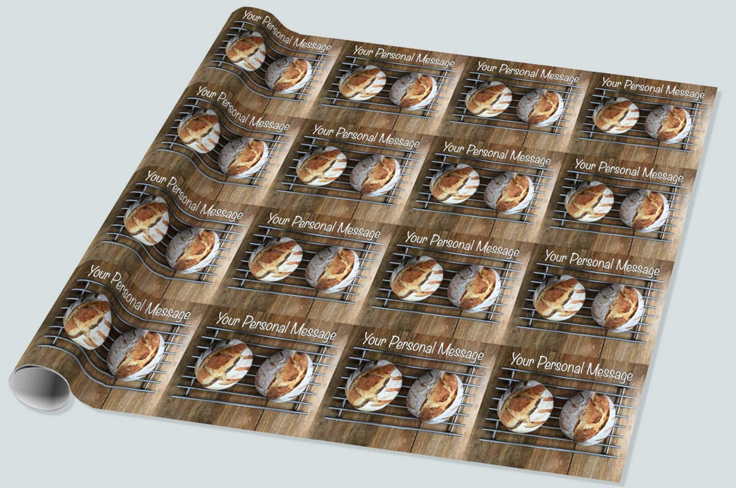 A roll of wrapping paper showing a pair of sourdough loaves resting on a metal tray upon a brown wooden table, along with a personal message, the image repeated in a mosaic pattern