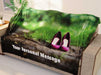 A blanket with an image of a pair of purple high heel shoes standing on a woodland path, the blanket is draped over a couch and there is a personal message printed