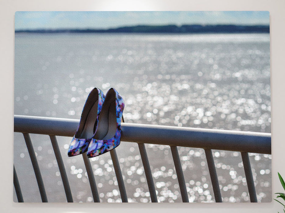 A pair of purple shoes sat on a blue metal fence on the shore of an ocean, with the ocean sparkling in the background