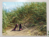 A pair of multicoloured shoes sat on sand on a beach, with sand dunes with grass in the background