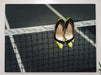 A pair of yellow high heel stiletto shoes hung on a tennis net