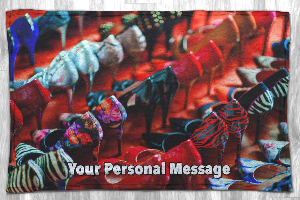 A blanket with an image of lots of high heel shoes in multiple rows, along with a personal message, the blanket is lying flat on a floor