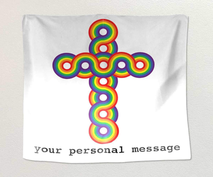 A tapestry hung on a white wall, the tapestry has a rainbow coloured crucifix on a white background, along with a personal message printed