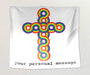 A tapestry hung on a white wall, the tapestry has a rainbow coloured crucifix on a white background, along with a personal message printed